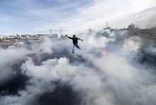 A Palestinian protester jumps as tear gas fired by Israeli soldiers rises during clashes in Jalazoun refugee camp near the West Bank city of Ramallah