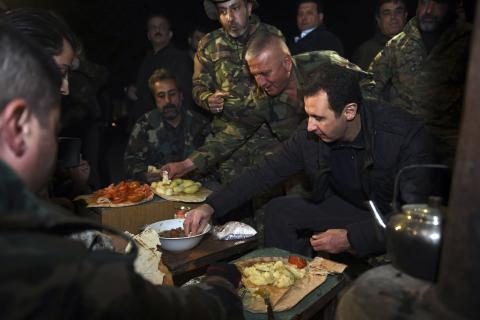 Syrian President Bashar al-Assad (R) eats with soldiers during a visit to Jobar, northeast of Damascus, in this handout photograph distributed by Syria's national news agency SANA, January 1, 2015. PHOTO BY REUTERS/SANA