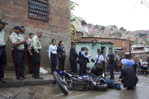 Police officers inspect the body of a dead gunshot victim on a street in Caracas