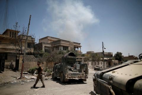 A member of the Iraqi rapid response forces walks past armoured vehicles as smoke rises in the background at the frontline in western Mosul, Iraq, June 4, 2017. PHOTO BY REUTERS/Alkis Konstantinidis