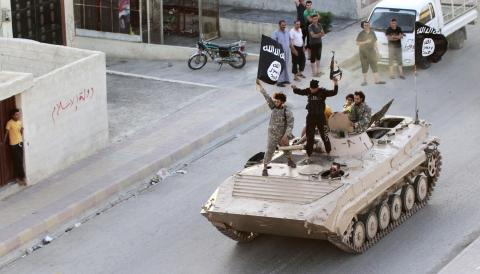 Militant Islamist fighters hold the flag of Islamic State (IS) while taking part in a military parade along the streets of northern Raqqa province, June 30, 2014. PHOTO BY REUTERS/Stringer