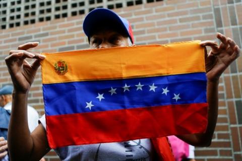 A woman holds a Venezuelan flag outside a validation center during Venezuela’s National Electoral Council (CNE) second phase of verifying signatures for a recall referendum against President Nicolas Maduro in Caracas, Venezuela, June 20, 2016. PHOTO BY REUTERS/Ivan Alvarado