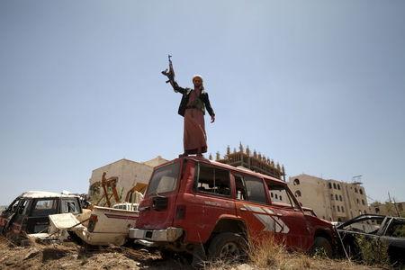 A follower of the Houthi group raises his weapon as he stands on a vehicle on a damaged street, caused by an April 20 air strike that hit a nearby army weapons depot, in Sanaa, April 21, 2015. PHOTO BY REUTERS/Mohamed al-Sayaghi