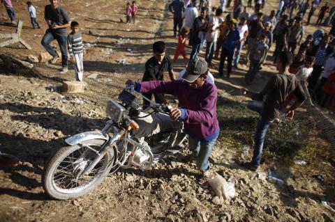 A Syrian Kurd pushes his motorcycle as he crosses into Turkey on the Turkish-Syrian border, near the southeastern town of Suruc in Sanliurfa province