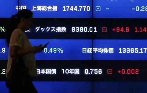A woman walks past a screen showing market indices in Tokyo