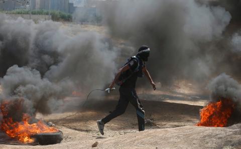 A Palestinian demonstrator drags a burning tire during a protest against U.S. embassy move to Jerusalem and ahead of the 70th anniversary of Nakba, at the Israel-Gaza border, east of Gaza City, May 14, 2018. PHOTO BY REUTERS/Mohammed Salem