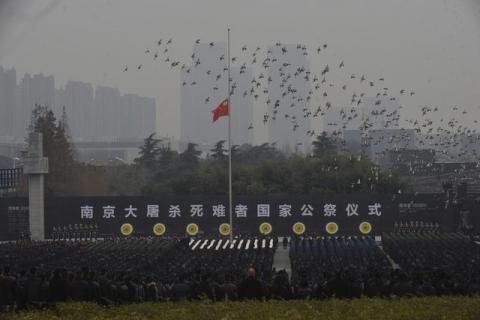 Pigeons fly above a Chinese flag flown at half-staff as people attend a ceremony to mark the second national memorial day for the Nanjing Massacre, at the Nanjing Massacre Museum in Nanjing, Jiangsu province, China, December 13, 2015. PHOTO BY REUTERS/China Daily