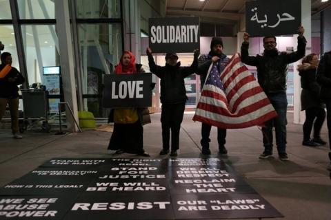 Protesters hold signs in opposition to U.S. President Donald Trump's ban on immigration and travel outside Terminal 4 at JFK airport in Queens, New York City, New York, U.S., January 29, 2017. PHOTO BY REUTERS/Joe Penney