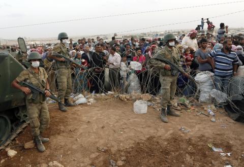 Turkish soldiers stand guard as Syrian Kurdish refugees wait behind the border fences to cross into Turkey near the southeastern town of Suruc in Sanliurfa province
