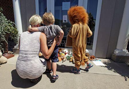 Sarah Madison (L) holds her son Beckett, 3, as her daughter Quinn, 5 (in costume), look at stuffed animals at the doorway of River Bluff Dental clinic in protest against the killing of "Cecil" a famous lion in Zimbabwe, in Bloomington, Minnesota July 29, 2015. PHOTO BY REUTERS/Eric Miller