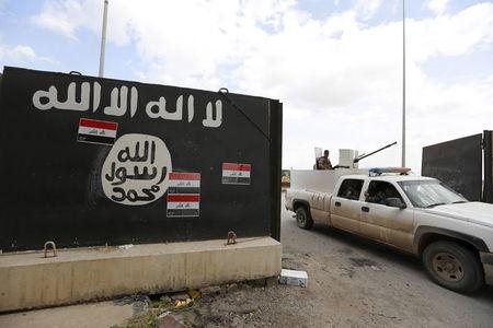 Iraqi security forces ride a vehicle past a wall painted with the black flag commonly used by Islamic State militants, near former Iraqi president Saddam Hussein's palace in Tikrit, April 1, 2015. PHOTO BY REUTERS/Thaier Al-Sudani