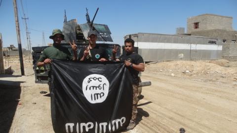 Iraqi security forces stand with an Islamic State flag which they pulled down in the town of Hit in Anbar province, April 2, 2016. PHOTO BY REUTERS/Stringer