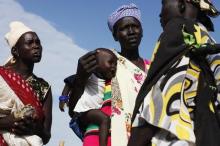 A woman carries a baby as she talks with other women talk at a food distribution in Minkaman, Lakes State, June 27, 2014. PHOTO BY REUTERS/Andreea Campeanu