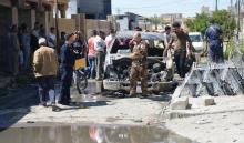 Iraqi people with security forces walk near a burnt vehicle at the site of an attack in Tikrit, Iraq, April 5, 2017. PHOTO BY REUTERS/Stringer