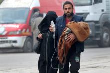 A man carries a child with an IV drip as he flees deeper into the remaining rebel-held areas of Aleppo, Syria, December 12, 2016. PHOTO BY REUTERS/Abdalrhman Ismail