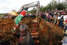 A man carries the national flag as coffins are arranged inside a mass grave during the burial of people killed when a dam burst its walls, overrunning nearby homes, in Solai town near Nakuru, Kenya, May 16, 2018. PHOTO BY REUTERS/Thomas Mukoya
