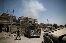 A member of the Iraqi rapid response forces walks past armoured vehicles as smoke rises in the background at the frontline in western Mosul, Iraq, June 4, 2017. PHOTO BY REUTERS/Alkis Konstantinidis