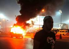 A soccer fan is seen near a police car, which was set on fire by fireworks, during clashes between soccer fans and security forces in front of a stadium on the outskirts of Cairo, February 8, 2015. PHOTO BY REUTERS/Stringer