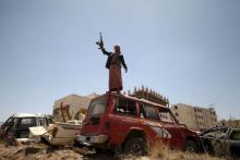 A follower of the Houthi group raises his weapon as he stands on a vehicle on a damaged street, caused by an April 20 air strike that hit a nearby army weapons depot, in Sanaa, April 21, 2015. PHOTO BY REUTERS/Mohamed al-Sayaghi