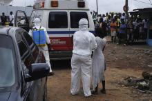 Health workers bring a woman suspected of having contracted Ebola virus to an ambulance in front of a crowd in Monrovia, Liberia