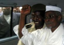 Former Chad President Hissene Habre (R) raises his fist in the air as he leaves a court in Dakar escorted by a Senegalese policeman, November 25, 2005. PHOTO BY REUTERS/Aliou Mbaye