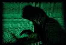 A hooded man holds a laptop computer as cyber code is projected on him in this illustration picture taken on May 13, 2017. PHOTO BY REUTERS/Kacper Pempel/Illustration