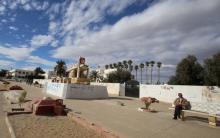 A man sits near to sculpture featuring a cart and symbolising poverty in Sidi Bouzid, Tunisia January 11, 2018. The slogan in Arabic reads 'What are we waiting for?'. Picture taken January 11, 2018. REUTERS/Amine Benaziza