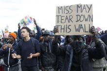 A migrant holds a placard with a message for Britain's prime minister as they face off with French riot police during a protest near the area called the "jungle" where they live in Calais, France, October 1, 2016. PHOTO BY REUTERS/Pascal Rossignol