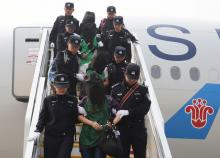 Police escort a group of people wanted for suspected fraud in China, after they were deported from Kenya, as they get off a plane after arriving at Beijing Capital International Airport in Beijing, China, April 13, 2016. PHOTO BY REUTERS/Yin Gang/Xinhua