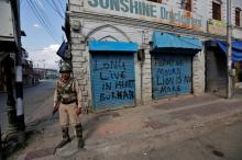 An Indian policeman stands guard in front of closed shops painted with graffiti during a curfew in Srinagar, July 12, 2016. PHOTO BY REUTERS/Danish Ismail