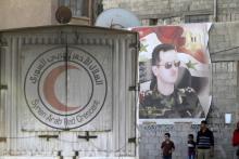 An aid convoy of the Syrian Arab Red Crescent enters the Wafideen Camp, which is controlled by Syrian government forces, near a poster of Syria's president Bashar al-Assad, to deliver aid into the rebel-held besieged Douma neighborhood of Damascus, Syria, March 4, 2016. PHOTO BY REUTERS/Omar Sanadiki