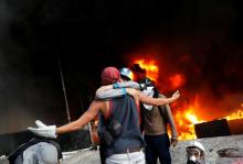 Protesters hug in front of a fire burning at the entrance of a building, housing the magistracy of the Supreme Court of Justice and a bank branch, during a rally against Venezuela's President Nicolas Maduro, in Caracas, Venezuela, June 12, 2017. PHOTO BY REUTERS/Carlos Garcia Rawlins
