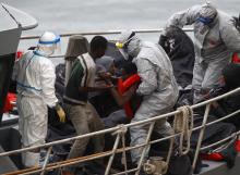 A rescued migrant and soldiers in biohazard suits help an ill migrant to his feet sit on an Armed Forces of Malta (AFM) patrol boat after arriving at the AFM's Maritime Squadron base at Haywharf in Valletta's Marsamxett Harbour, January 22, 2015. PHOTO BY REUTERS/Darrin Zammit Lupi