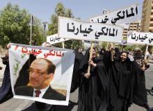 People hold a portrait of Nuri al-Maliki and signs as they gather in support of him in Baghdad