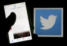 A man reads tweets on his phone in front of a displayed Twitter logo in Bordeaux, southwestern France, March 10, 2016. PHOTO BY REUTERS/Regis Duvignau