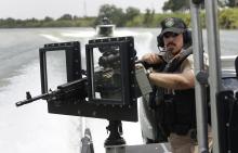 A Texas Parks and Wildlife warden stands next to a 30-caliber rifle as he patrols on the Rio Grande along the U.S.-Mexico border near Mission, Texas